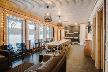 Aulanko Lake Villa's main hall. In the foreground, a sofa corner, in the middle a scenery bar counter and dining area, and in the back, a kitchen corner with access to the electric sauna compartment.